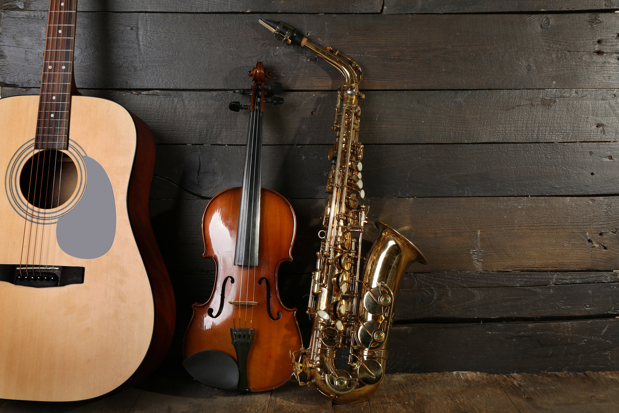 Gitarre, Geige und Saxophon lehnen an einer dunklen Holzwand